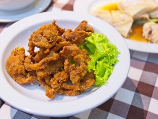 Crispy fried pork strips on a white plate decorate with green lettuce on red checked Pattern tablecloth