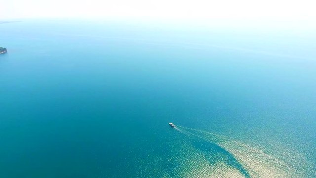 Fast moving speed boat wake on clear blue sea water, turquoise building, ship shore, waves, green forests, Mussera Pitsunda, Abkhazia. Aerial view: Drone Bird Eye View sideways motorboat tropical.