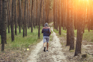 Obraz premium Man in a hoodie running in a pine forest. Concept of training in