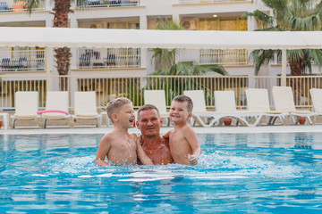Fototapeta premium cheerful children with their father jump in the outdoor blue pool on vacation