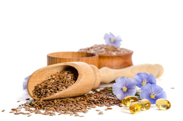  Flax seeds in the wooden scoop, bowl with oil and oil in caps and  beauty flowers isolated on white background. Phytotherapy.