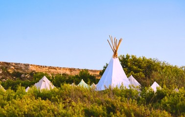 White canvas teepees (or wigwams) camped in a field under a clear blue sky