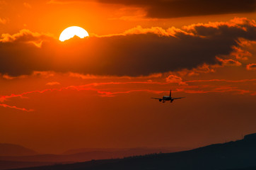 Fototapeta na wymiar Landing plane silhouette in sunset sky, sun ball, space for text