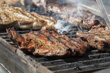 Meat steaks are cooked on a hot grill with smoke. Close-up