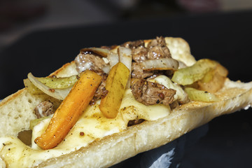Sandwich or burrito-roasted meat with vegetables and cheese inside a fresh white loaf on a dark background