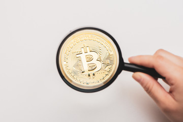 A gold bitcoin under magnifying glass.