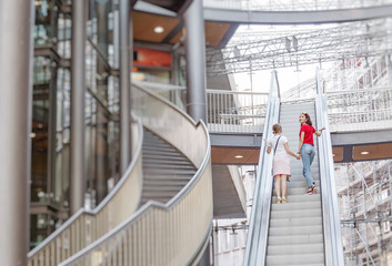 happy young woman friends on escalator in shopping mall