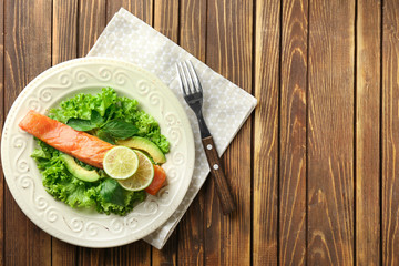 Plate with tasty salmon and fresh salad on wooden table
