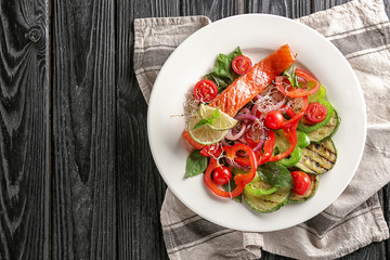 Plate with tasty salmon and fresh salad on wooden table