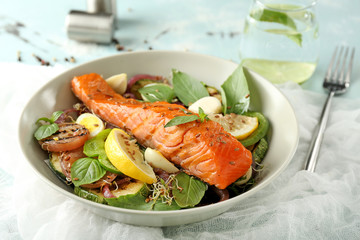 Plate with tasty salmon and fresh salad on light table