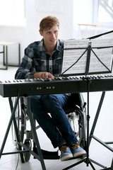 Young musician in wheelchair playing synthesizer at home