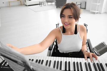 Beautiful young musician in wheelchair playing synthesizer at home