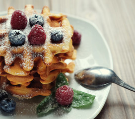 Belgian waffles with blueberries, raspberries and powdered sugar on wooden table