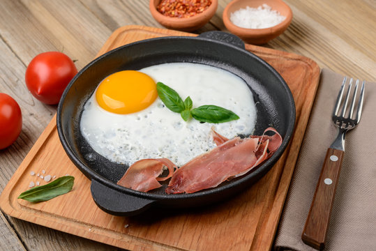 Fried egg in a pan with bacon and  tomatoes  on  rustic wooden  background.