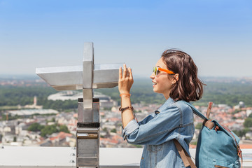 Woman looking in binoculars enjoying cityscape view through city Telescope
