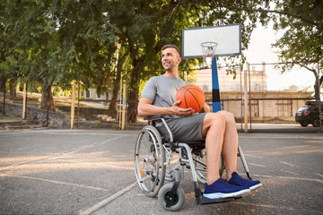 Sporty young man with ball sitting in wheelchair outdoors