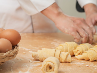 Chef hands are rolling a croissant from dough on wooden board. black background.