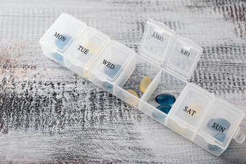 Plastic container with pills on wooden background