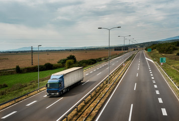 Blue lorry truck driving on asphalt highway road with High-mast lighting in a pastoral landscape