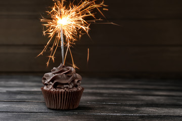 Tasty chocolate cupcake with sparkler on wooden table