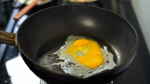 slow-motion of hand cracking egg dropping into a frying pan