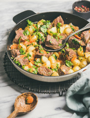 Meat dinner. Braised beef meat with potato and carrot with fresh parsley in cooking pan over white marble table background, selective focus. Comfort winter food