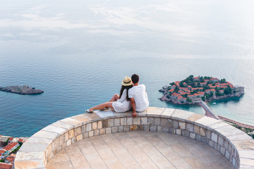 couple hugging on viewpoint and looking at island of Sveti Stefan in Budva, Montenegro