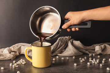 Fototapeta na wymiar Woman pouring hot chocolate from pot into metal cup on dark table