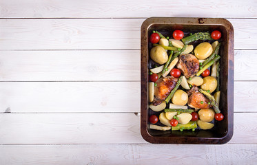 Baked in oven potato, chiken, asparagus, cherry tomato in baking pan over on white wooden background. Overhead. Copy space.