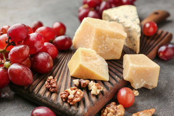 Wooden board with cheese, ripe juicy grapes and nuts on grey table