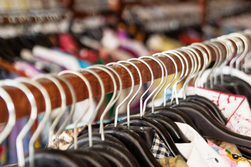 Wooden clothes racks with hangers and with colorful clothes on a blurred background inside shop.