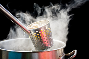 Noodles in the basket, that blanched in a hot noodle aluminium pot with white smoke and steam on...
