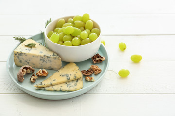 Bowl with ripe juicy grapes and cheese on white wooden table