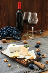 Fototapeta na wymiar Wooden board with different types of cheese, ripe grapes and nuts on table