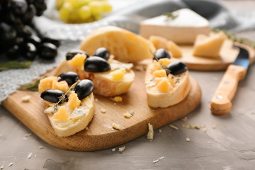 Tasty sandwiches with cheese and grapes on wooden board