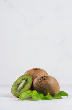 Ripe fleshy green kiwi with juicy slice, young leaves on soft light white table, vertical. Tropical fruits background.