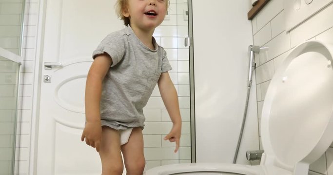 Kid boy climbs on the toilet, prepares to makes to toilet the white interior bathroom