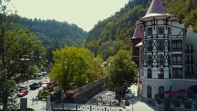 Aerial drone flight up from the river Borjomka close to pine and deciduous trees growing on the sides, Borjomi park in gorge between mountains in sunny day, bridge across the parched river, Georgia