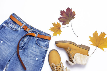 Female blue jeans, boots and autumn leaves on green background top view flat lay. Fashion Lady Clothes Set Trendy Cozy Knit Jumper Autumn accessories Female fashion look