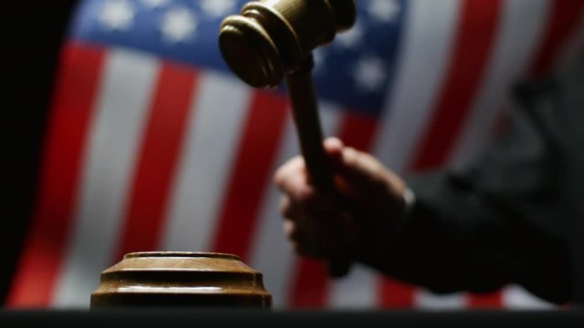 Judge hammering with wooden gavel against waving American flag in USA court room