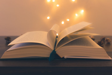 Open book on a wooden table with yellow lights coming out of its pages