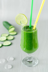 A glass of green vegetable smoothies on a white wooden background, and pieces of ice on the table