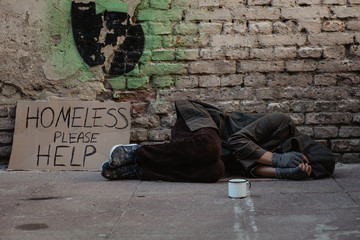 Homeless man lies on the street in the shadow of the old building and begging for help and money....