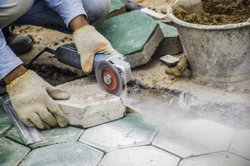 The workers cutting green concrete hexagonal blocks for paving.