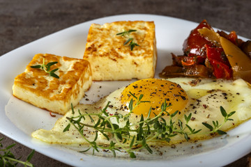 Fried egg with fried cheese, butter and some pickles on the plate