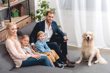 high angle view of happy young family sitting on couch at home with dog and looking at camera