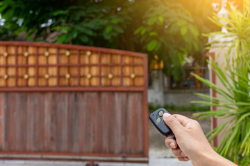 Female hand holding and using remote control to open or close the automatic wooden gate with home...