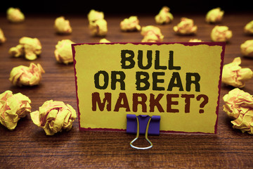 Naklejka premium Handwriting text writing Bull Or Bear Market question. Concept meaning asking someone about his marketing method Yellow sticky card clipped text notice crumpled paper balls wood table