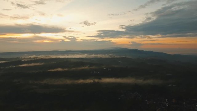 Aerial view of mystical, foggy forest forest, mountains with fog, clouds at sunset on Bali,Indonesia. Tropical rainforest, trees, jungle in mountains. Fog over the jungle. Travel concept. Aerial