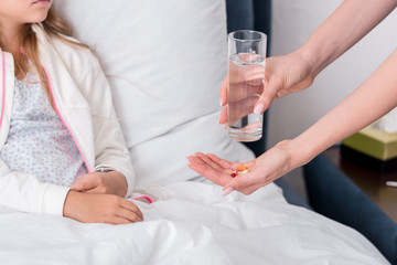 cropped shot of mother giving pills and water to her sick daughter in bed